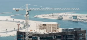 Building construction project in Sharjah with a tower crane overlooking the waterfront.