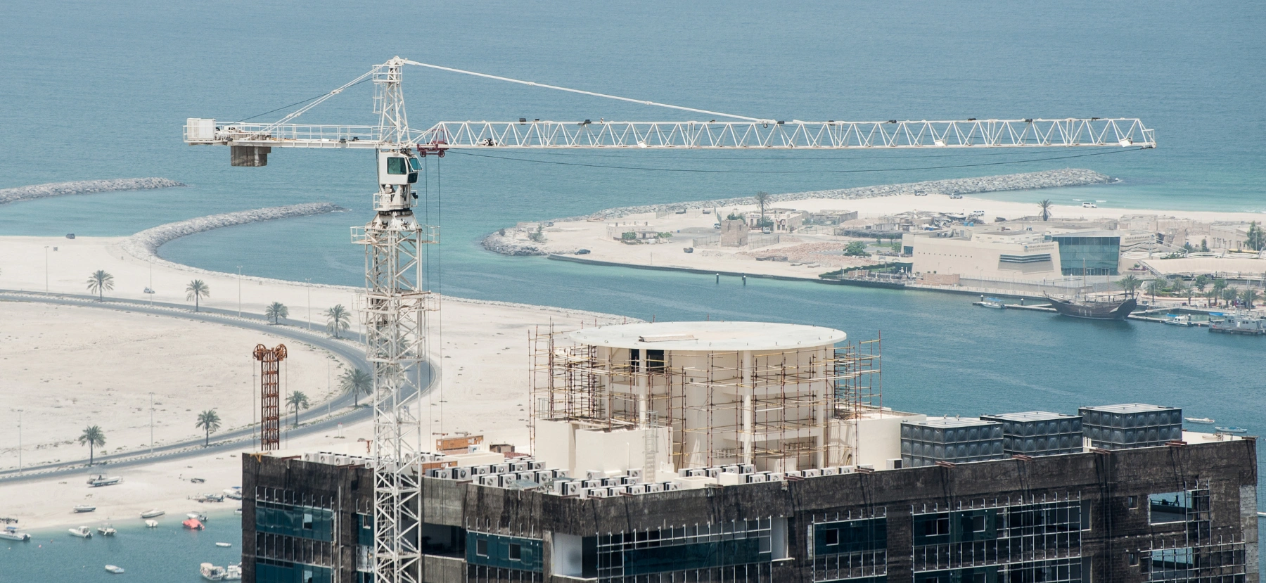 Building construction project in Sharjah with a tower crane overlooking the waterfront.